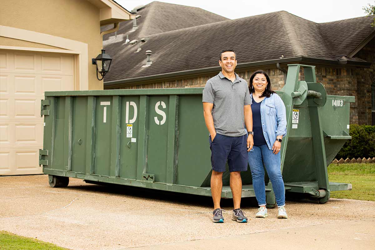 a couple in front of a mini dumpster in front of their house