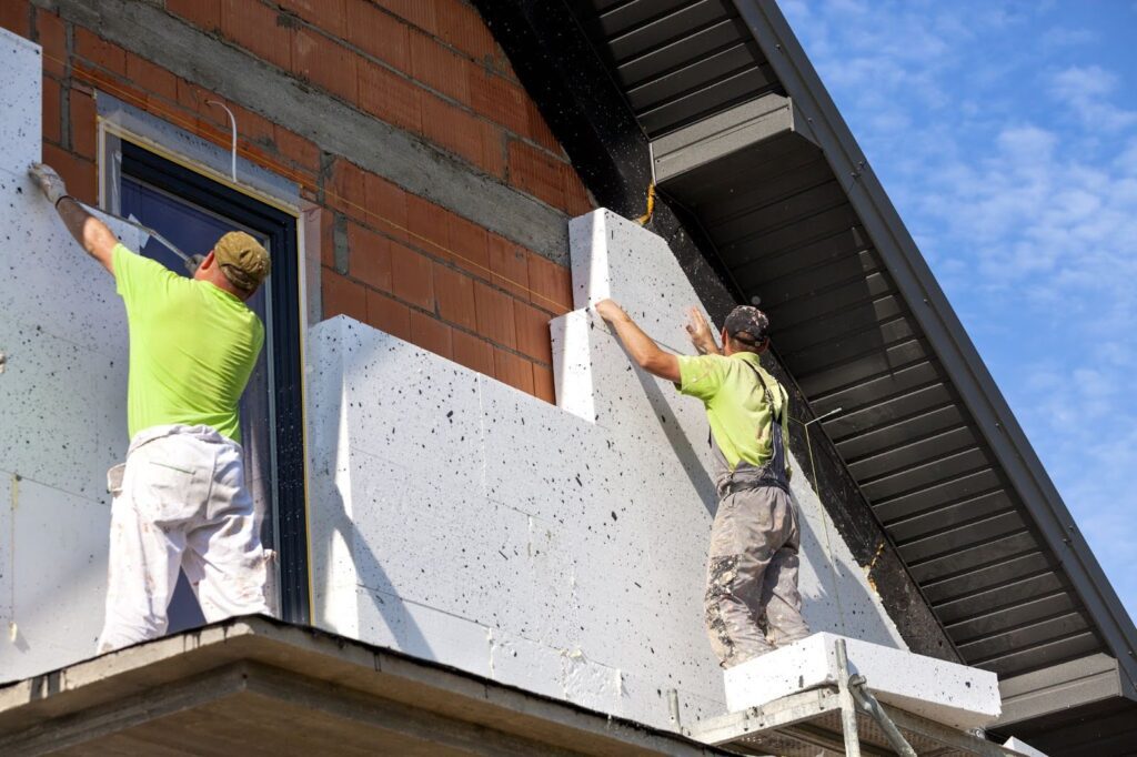 Two workers installing styrofoam in home exterior.